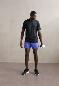 Schwarzes, kurzärmeliges Sportoberteil, blaue Shorts und schwarze Turnschuhe; hält ein Hantel. Glatte Texturen, einfaches Design und keine Muster.