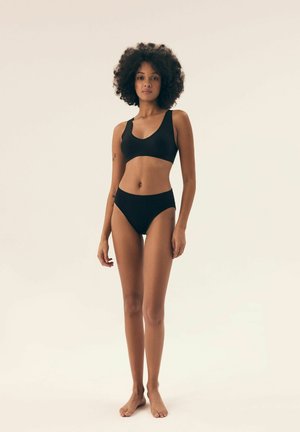 Czarny stanik i wysoki stanik bikini, wykonane z miękkiego materiału. Stanik ma dekolt w kształcie łódki i szerokie ramiączka, oferując minimalne pokrycie.