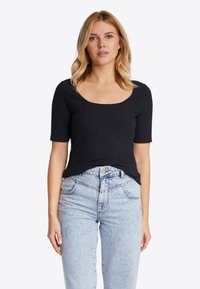 Top corto a maniche corte nero a coste con scollatura a barca, abbinato a jeans in denim azzurri a vita alta con tasche frontali e chiusura a bottone.