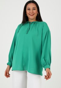 Grüne Bluse mit einem runden Ausschnitt, Bindeband und langen Ballonärmeln. Aus glattem Stoff gefertigt, hat sie eine lockere Passform und einen abgerundeten Saum.