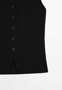 Black ribbed tank top with six black buttons in a vertical line, featuring a side slit at the hem for added detail.