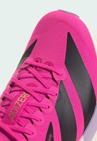 Ružičasta atletska cipela s teksturiranim gornjim dijelom, crnim akcentima i odvažnim logotipom "ADIZERO". Ima ravne vezice i dizajn s okruglim vrhom.