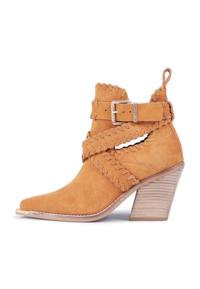 Bottine en daim tan avec un bout pointu, des bords à franges, des sangles décoratives et un talon empilé. Comprend une boucle latérale et des détails ajourés.