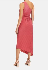 Vestido midi de canalé de un solo hombro en color coral, con una parte trasera drapeada, dobladillo asimétrico y textura suave. Combinado con sandalias de tacón cuadrado en tono nude.