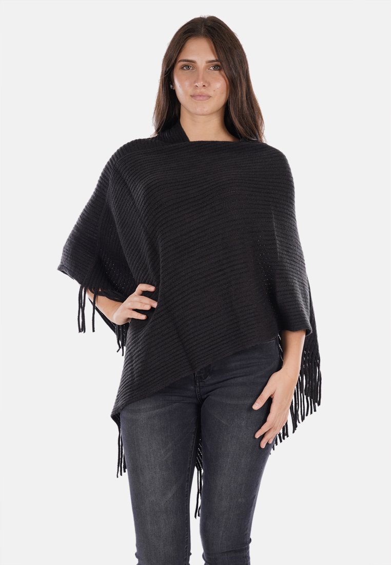 Poncho nero lavorato a maglia con un motivo testurizzato, caratterizzato da orli frangiati e un design loose e asimmetrico. Indossato su jeans scuri.