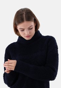 Marineblaues, strukturiertes Pullover-Sweatshirt mit hohem Kragen und langen Ärmeln, gefertigt aus einem gemütlichen, weichen Material und mit gerippten Bündchen.