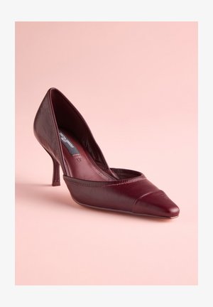 Pantof cu toc din piele vișinie, cu vârf ascuțit și detaliu curbat cu bretea, având un toc subțire și un finisaj subtil texturat.