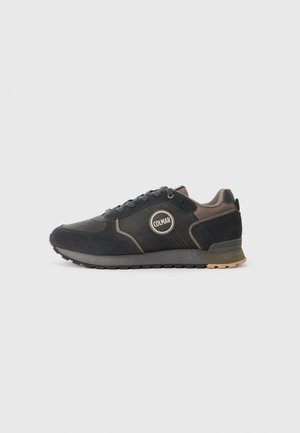Schwarze SportSneaker aus einer Kombination von Wildleder und synthetischen Materialien, ausgestattet mit einem runden Logo, Schnürdesign und Gummisohle.