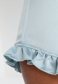 Light blue garment featuring a smooth texture with a ruffled hem. The design shows a close-up of the hem's detailed stitching and finish.
