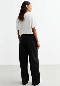 Witte korte mouwen top gecombineerd met zwarte losse broek. De broek heeft een elastische tailleband. Minimalistisch ontwerp, gladde textuur.