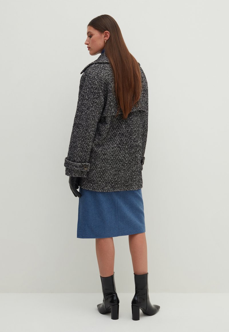 Cappotto a zigzag bianco e nero con ampio colletto, maniche con risvolto e bottoni, abbinato a una gonna blu e stivali neri con tacco.