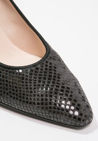 Chaussure en cuir verni noir avec un bout pointu, présentant un motif reptile texturé et une doublure intérieure lisse. Bordée d'un contour noir.