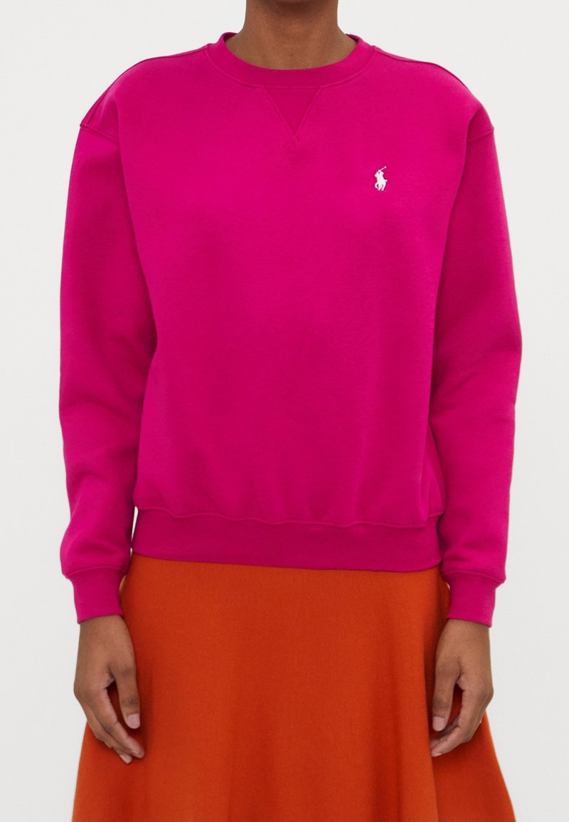 Rosa sweatshirt med rund halsringning och ribbade muddar. Har en liten vit broderad logga på vänster bröst och en avslappnad passform.