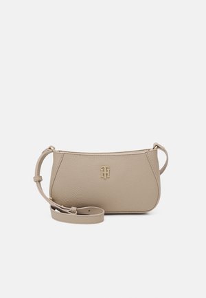 Beige leren crossbodytas met verstelbare riem en goudkleurig logo van dubbele initialen aan de voorkant, afgebeeld tegen een witte achtergrond.