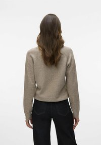 Beige wool sweater with a relaxed fit, featuring long sleeves, a round neck, and ribbed cuffs, worn with dark blue jeans.