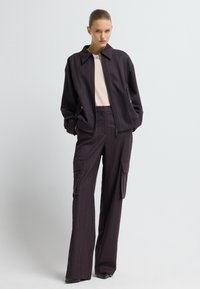 Chaqueta morada oscura con cremallera y diseño tipo cuello. Pantalones cargo de pierna ancha a juego, con bolsillos, tela texturizada y patrón de rayas.