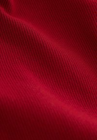 Rødt stof med et tekstureret ribbet mønster, der har en subtil glans og fine detaljer. Overfladen fremstår glat med varierende lys og skygge.