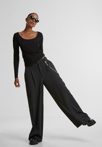 Un top negru cu mânecă lungă, combinat cu pantaloni largi în dungi negre și albe, având un detaliu din lanț argintiu. Topul este ajustat, iar pantalonii au un croi lejer.