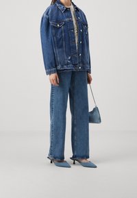 Jeansjacka och vida jeans i blått, tillsammans med ljusblå klackmules och en liten handväska, vilket skapar en monokromatisk look.