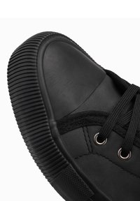 Schwarzer Sneaker mit Gummispitze, strukturiertem Sohle, schwarzen Schnürsenkeln und metallischen Ösen; aus glattem Material mit matter Oberfläche.