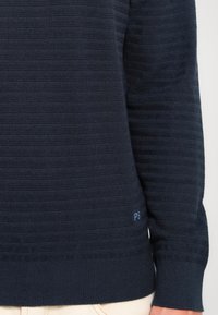 Tummansininen teksturoitu neulepaita, jossa on vaaka-ristikkokuvio. Paita sisältää pienen "PS"-logon vasemmalla puolella helmassa.