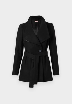 Manteau pour femme noir à ceinture, avec de larges revers, fermeture à un bouton et accents métalliques aux extrémités de la ceinture et à la broche de revers.
