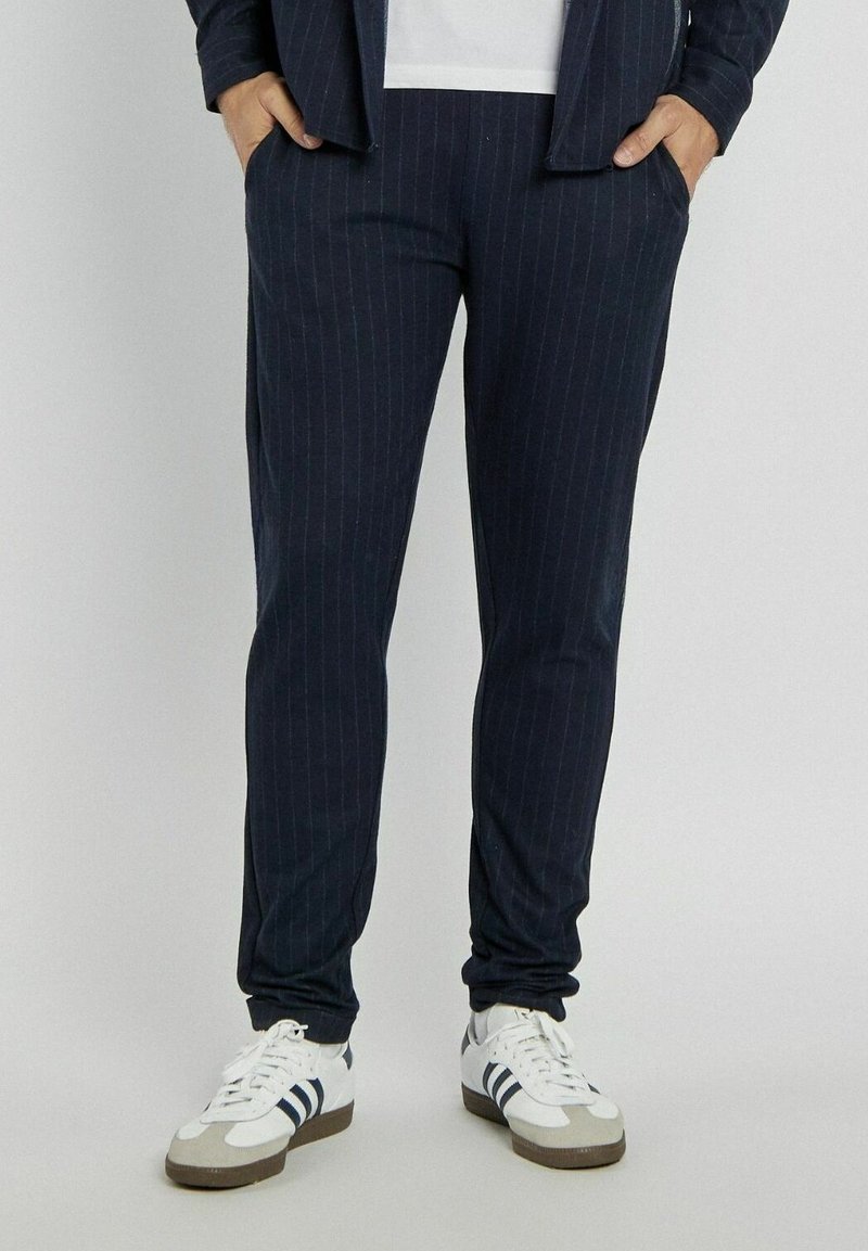 Granatowe spodnie w paski o slim fit, z bocznymi kieszeniami i miękką strukturą materiału, połączone z białymi sneakerami i szarymi akcentami.