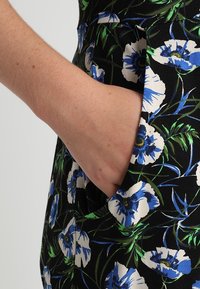 Robe florale avec un fond noir et des motifs de fleurs bleues et blanches, à manches courtes, et une poche sur le côté.