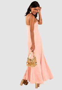 Langes pinkes Kleid mit dünnen Trägern, fließendem Stoff und ausgestellt geschnittenem Saum. Die Accessoires umfassen eine goldene Handtasche und Plateauschuhe.