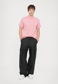 T-shirt en coton rose clair à manches courtes avec un petit logo. Pantalons cargo noirs à jambes larges avec poches latérales et baskets blanches.
