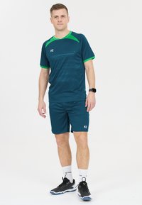 Mörk teal sportoutfit med gröna detaljer, korta ärmar och shorts, med "FZ"-logotypen på båda delarna. Bärs med svarta träningsskor.