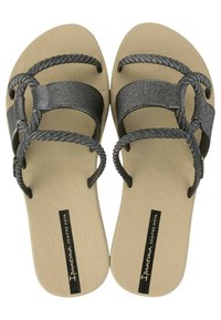 Flip-flop neri e argento con design della fascia intrecciata, suola piatta beige con motivo testurizzato e logo stampato sulla pianta.