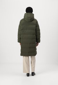 Dark green puffer coat with a hood, featuring horizontal quilted sections and a mid-calf length, paired with cream wide-leg pants and black boots.