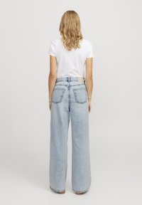 Jeans azzurri a gamba larga con vita alta, tasche posteriori e una texture sottile. Abbinati a una maglietta bianca semplice.