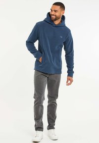 Blauwe fleece hoodie met een voorzak, lange mouwen en een capuchon met trekkoord. Gecombineerd met grijze jeans en witte sneakers.