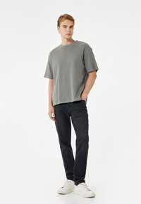 Grå kortærmet t-shirt med en afslappet pasform, parret med sorte jeans og hvide sneakers. Glat tekstur, minimalistisk design.