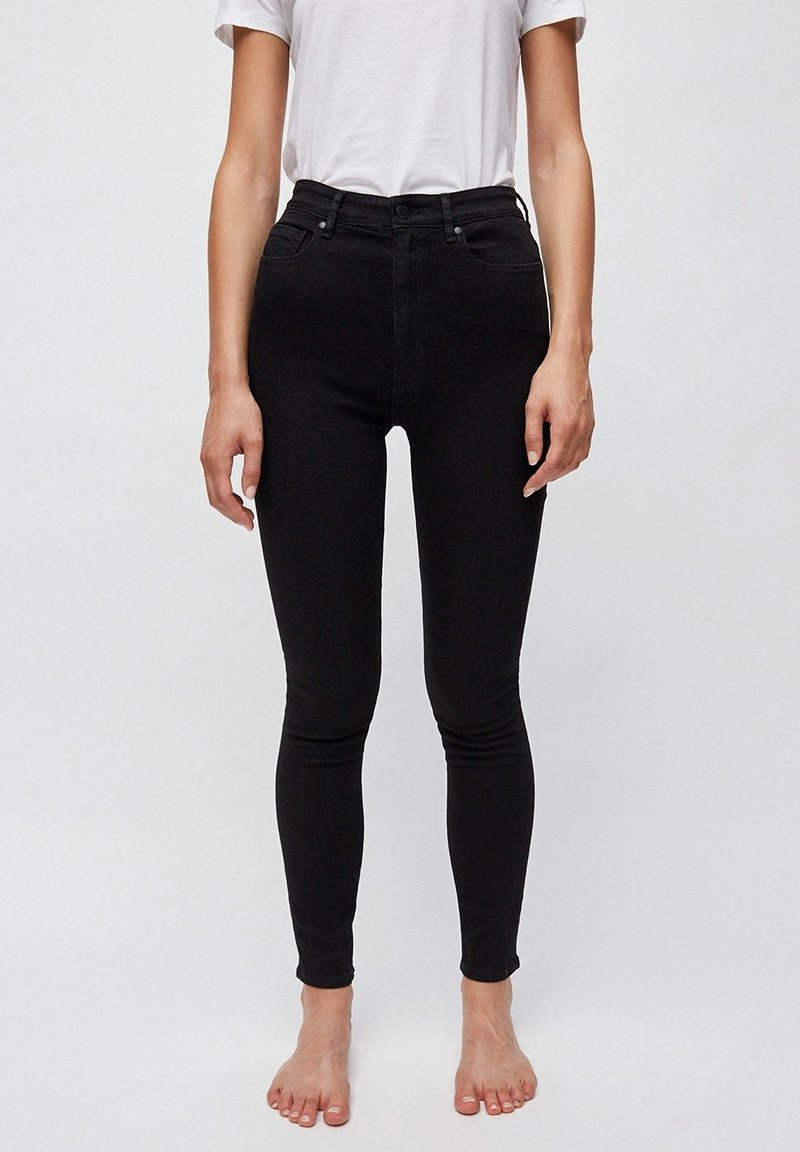 Jean noir taille haute en denim, présentant une silhouette ajustée, deux poches avant et un matériel minimaliste avec une finition lisse.