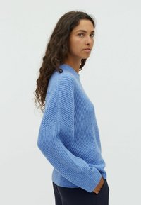 Pull en maille côtelée bleu clair avec une coupe décontractée, un col rond et des manches longues, présentant un motif texturé et un tissu doux.