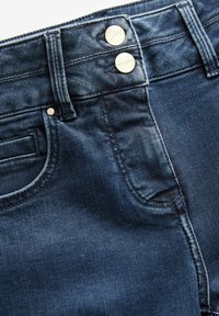 Jeans in denim blu scuro con una consistenza liscia, due bottoni metallici visibili in vita e un classico design a cinque tasche.