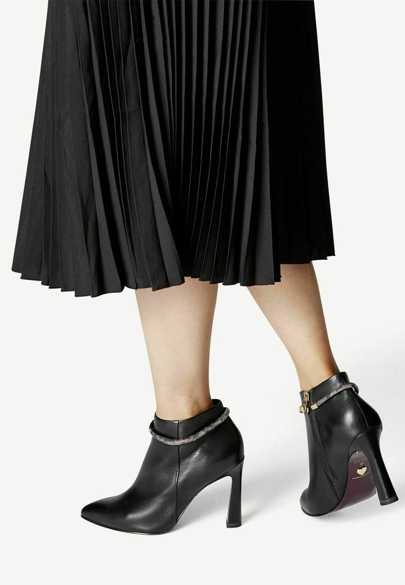 Svarta läderankelboots med spetsig tå och hög stilettklack; prydda med en kedjedetalj runt ankeln.