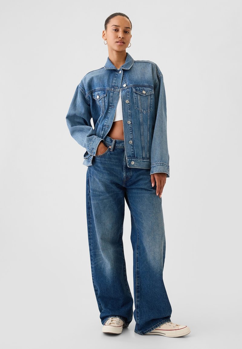 Džinsinis švarkas su atvartais ant apykaklės, užsegamas sagomis priekyje, su krūtinės kišenėmis, derinamas su aukštu liemeniu ir plačiomis tiesiom kelnėmis bei drobiniais sportbačiais.