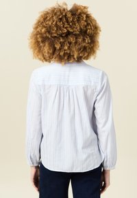 Camicia button-up a righe blu chiaro con dettagli nella parte posteriore e pieghe arricciate. Maniche lunghe con polsini abbottonati, tessuto dalla texture morbida.