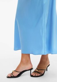 Blå satengkjole med et flytende design, kombinert med svarte remsandaletter med hæl og gullaccent på den fremre stroppen.