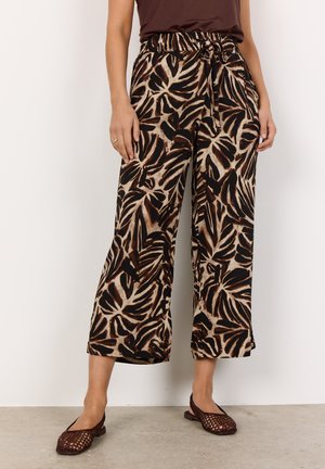 Höga, vida byxor i brunt och beiget tropiskt mönster. Tyget verkar lätt och har en strukturerad yta. Stylistiskt kombinerade med slip-on skor.