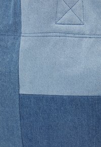 Denim-stof med et patchworkdesign i forskellige nuancer af blå. Inkluderer diagonal tekstur og synlige syninger.