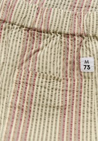 Material în dungi de culoare bej, roz și gri, cu o suprafață texturată. Dispune de un tiv elastic și o etichetă cu "M 73."