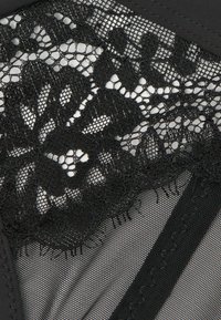 Zwarte kant bh met ingewikkelde bloemenpatronen, doorschijnende gaasdetails en een gladde stof met textuurachtige randen en stiksels.