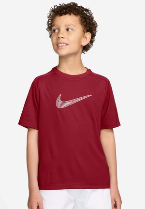 Jongen met krullend haar die een rood Nike T-shirt met wit logo draagt, kijkt opzij tegen een effen witte achtergrond.