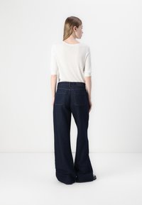 Bredde ben mørkeblå denim jeans med høy midje og baklommer, kombinert med en tettsittende hvit topp med korte ermer.