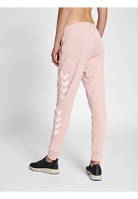 Ljusrosa joggingbyxor med en tapered passform, som har vita chevronmönster längs sidorna och elastiska muddar vid anklarna.